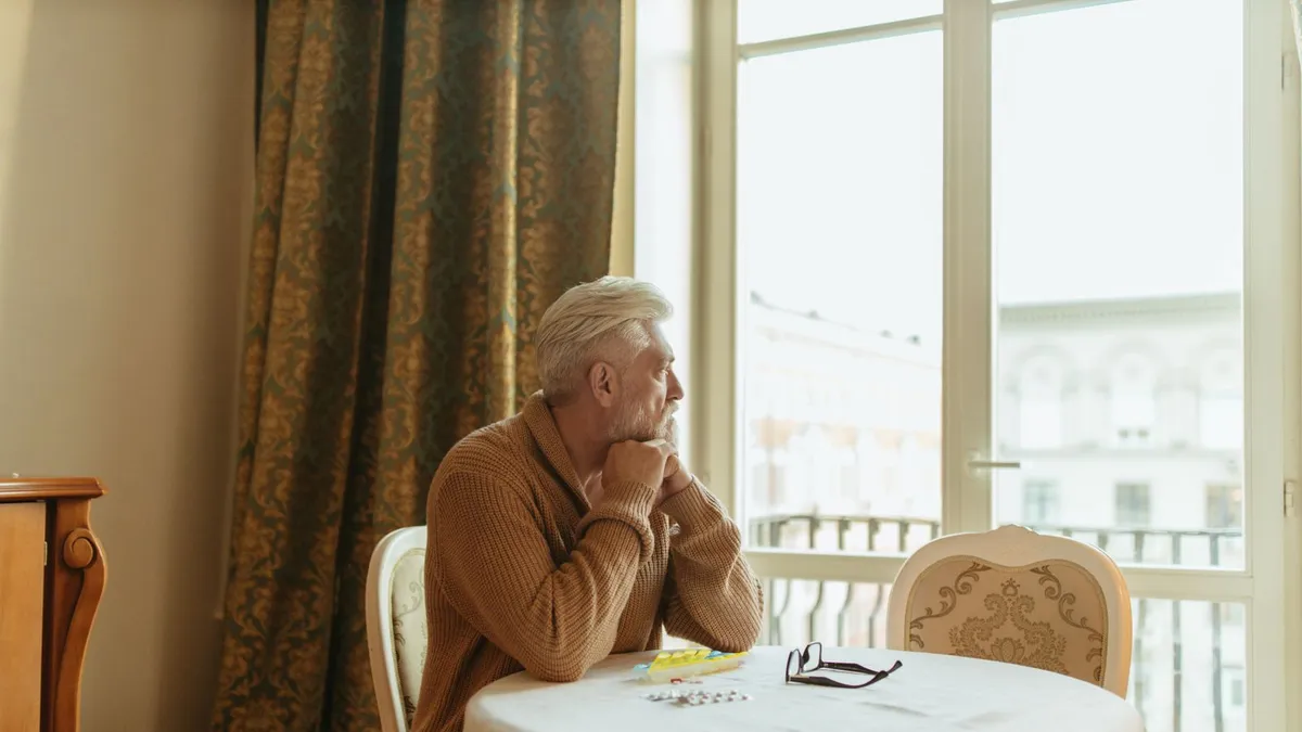 Man standing at a window thinking through which loan option fits while between jobs